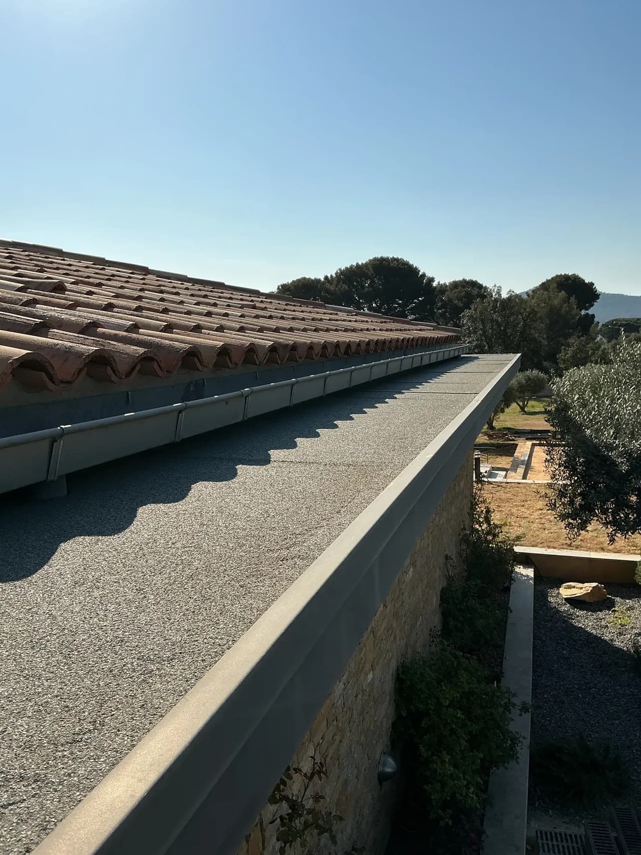 Étanchéité autoprotégée existante d'une casquette béton avant réfection, le long d'une toiture en tuiles anciennes