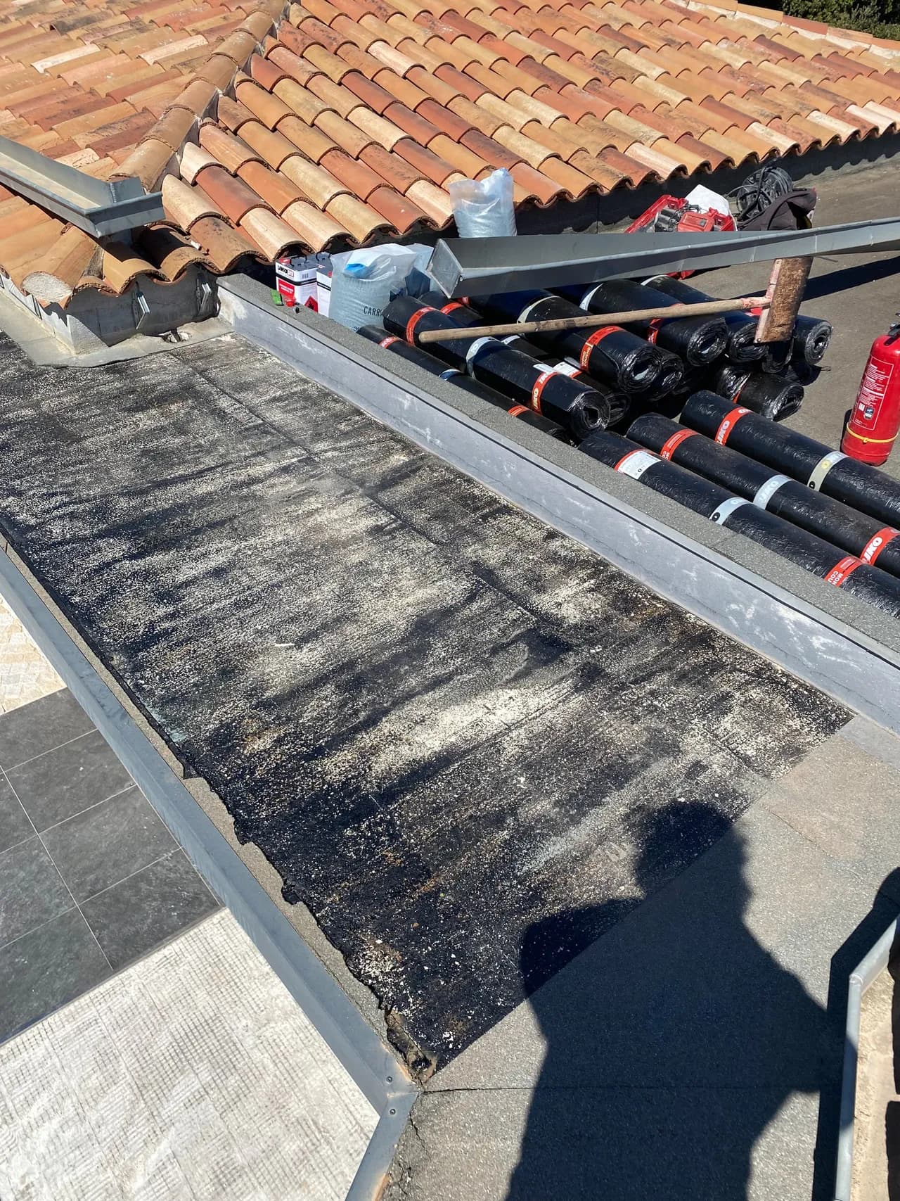 Ancienne étanchéité bitume usée d'une casquette béton avant dépose, rouleaux de membrane SBS prêts à poser